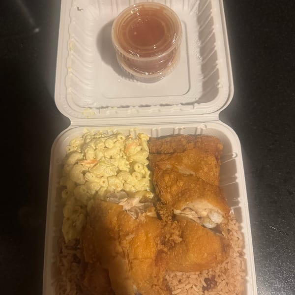 Fried chicken, rice and beans, and macaroni salad in a white takeout container with sauce cups.