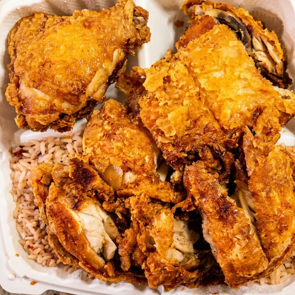 Crispy fried chicken pieces and rice in a white takeout container on a brown paper bag.