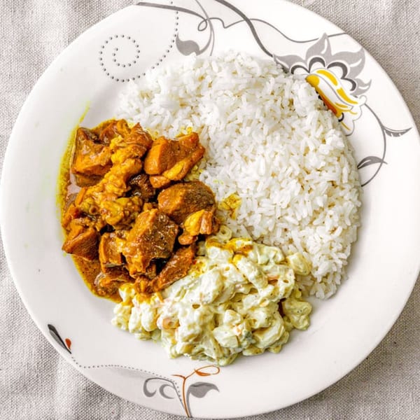 A plate of chicken curry, white rice, and macaroni salad on a white tablecloth.