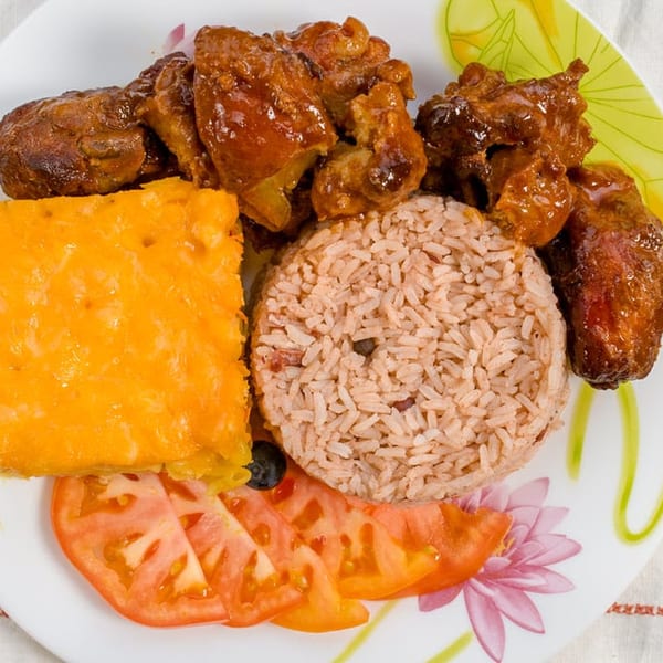 Plate of seasoned rice, glazed chicken, cheesy baked casserole, sliced tomatoes, and black beans on a floral dish.